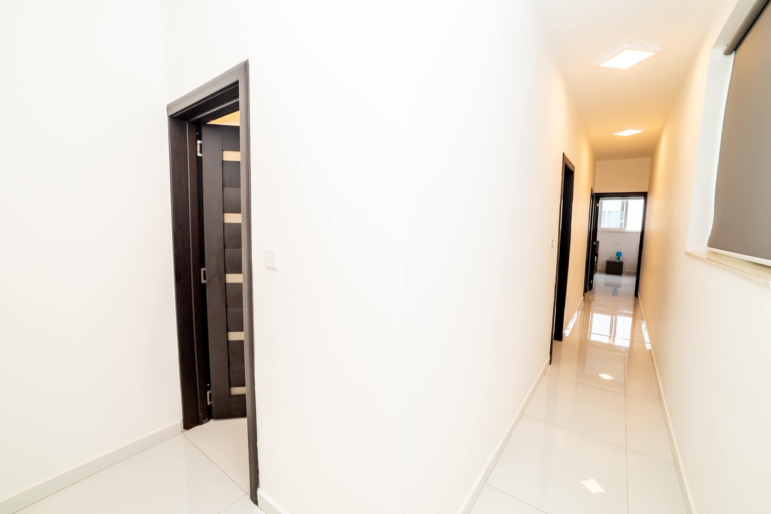 A hallway with a door leading to a room, a tiled floor, and a ceiling light.