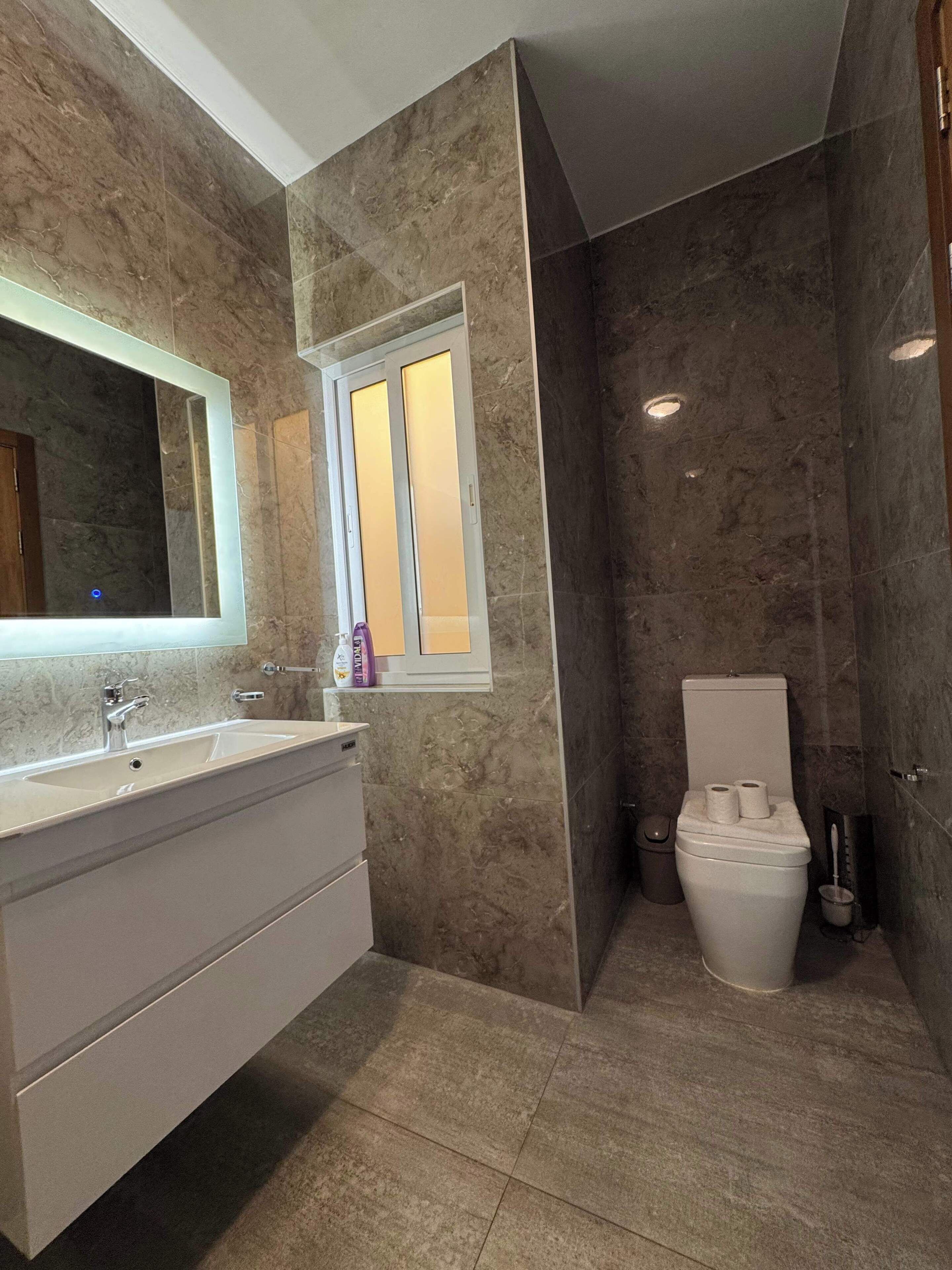 Ein modernes Badezimmer mit Marmorwaschtisch, großem Spiegel und Toilette.