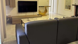 Una sala de estar moderna con un televisor de pantalla plana grande, un sofá, un reloj y un equipo de aire acondicionado.
