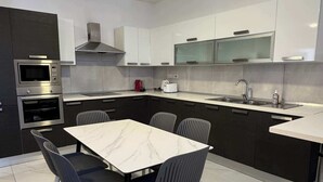 Una cocina moderna con armarios blancos, encimera de mármol y comedor con mesa blanca y sillas grises.