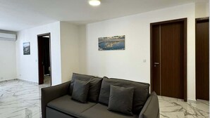 A spacious living room with a dark grey sofa, a marble floor, and a painting on the wall. - Modern 2-Bedroom Home – by HostMT (San Pawl il-Baħar)