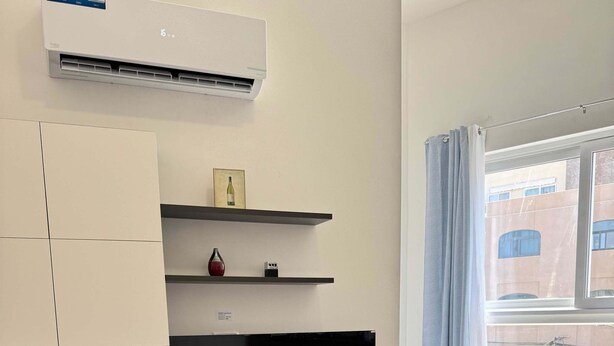 Un soggiorno moderno con una TV a schermo piatto, un divano, un tavolino da caffè e un condizionatore d'aria a parete.