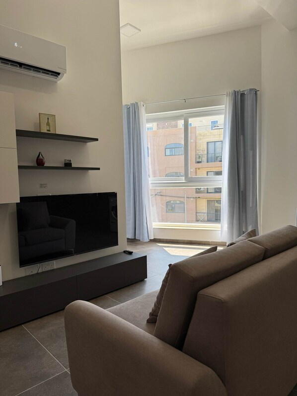 Una sala de estar moderna con una televisión de pantalla plana, un sofá y un ventanal con cortinas.