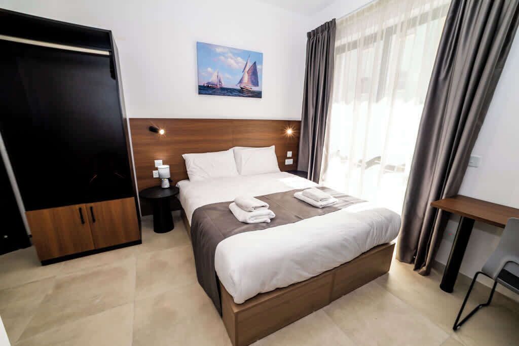 Una camera d'albergo con un letto, un comodino, una scrivania, una sedia, un armadio e un quadro appeso al muro.