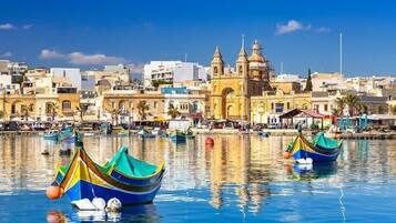 Una cittadina costiera con barche colorate ormeggiate nell'acqua, una chiesa importante con un campanile e un cielo azzurro limpido.