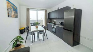 Una cocina moderna con un refrigerador de acero inoxidable, gabinetes oscuros y un comedor con mesa y sillas.