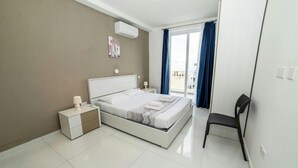 Un dormitorio moderno con cama, mesitas de noche, una silla y vistas al exterior.