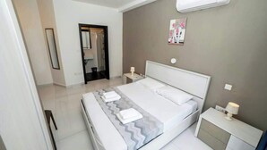 Una habitación de hotel moderna con una cama grande, una mesita de noche con una lámpara, aire acondicionado instalado en la pared y una puerta que da a un baño.