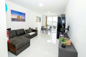 A modern living room with a sofa, a dining area, and a balcony with a view. - Modern 2BR Apartment with Terrace – by HostMT (San Pawl il-Baħar)