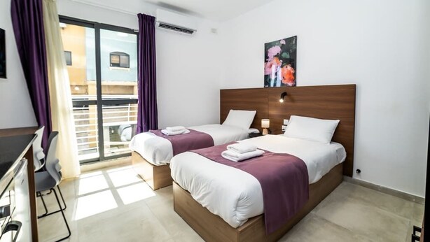 Ett hotellrum med två sängar, ett skrivbord och ett stort fönster med lila gardiner.