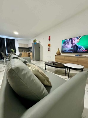 Un soggiorno moderno con un divano grigio, un tavolino da caffè e un televisore piatto che mostra un film.