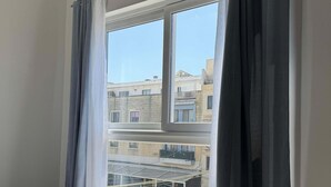 Um quarto com uma janela grande, cortinas cinzas e piso de azulejos.