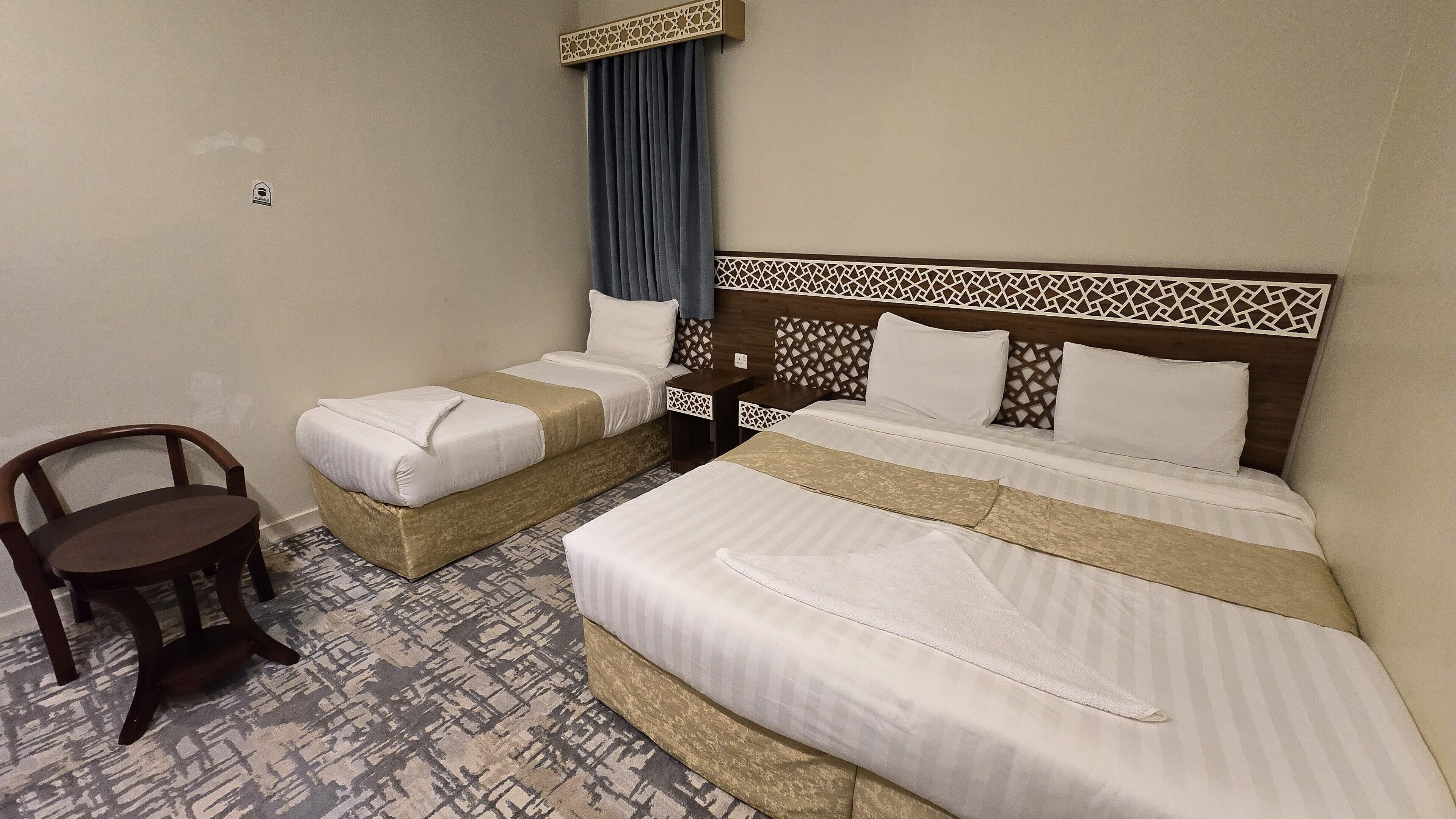 A hotel room with two single beds, a wooden chair, and a patterned carpet.