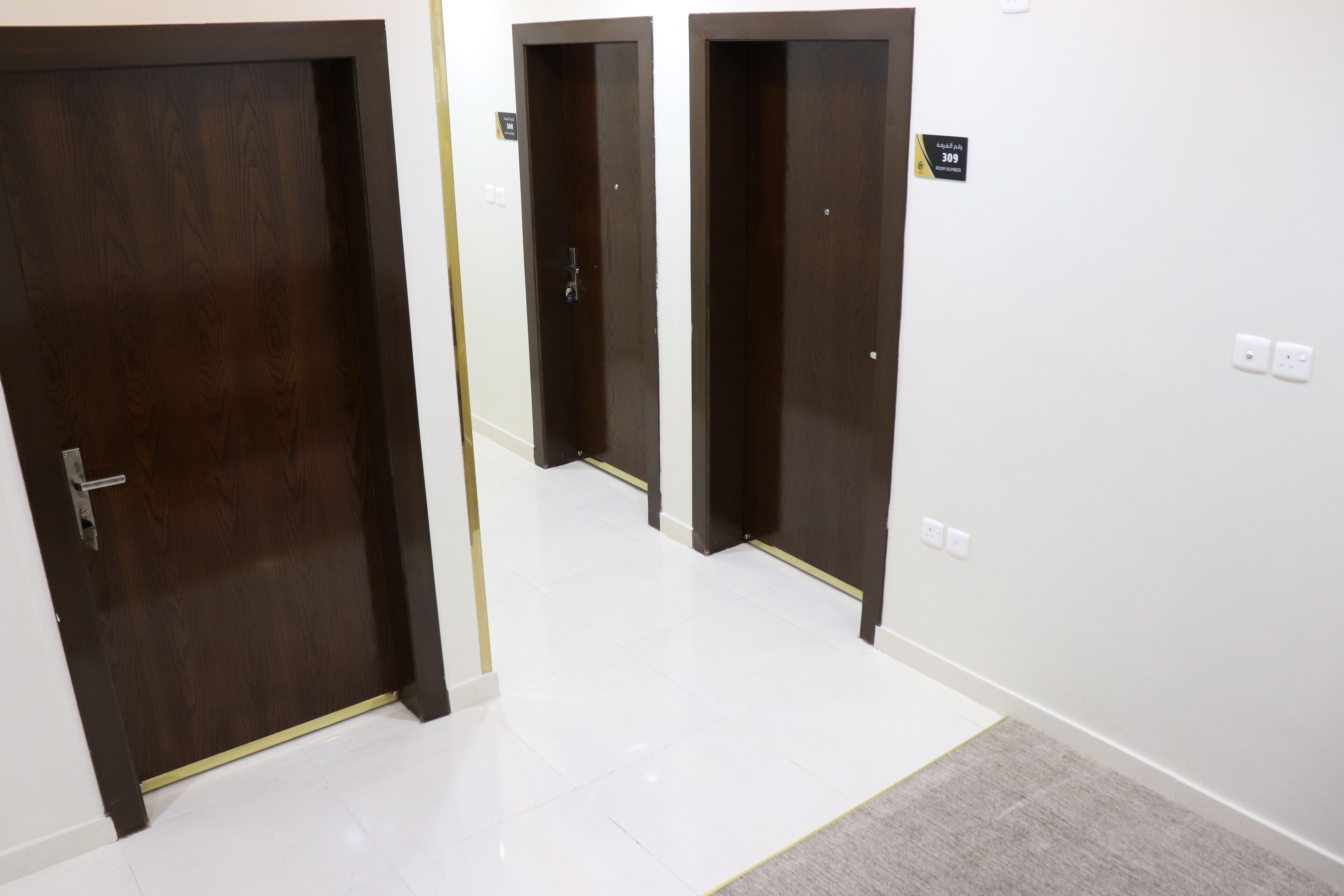 Um corredor com três portas de madeira, cada uma com uma placa indicando o número do quarto.