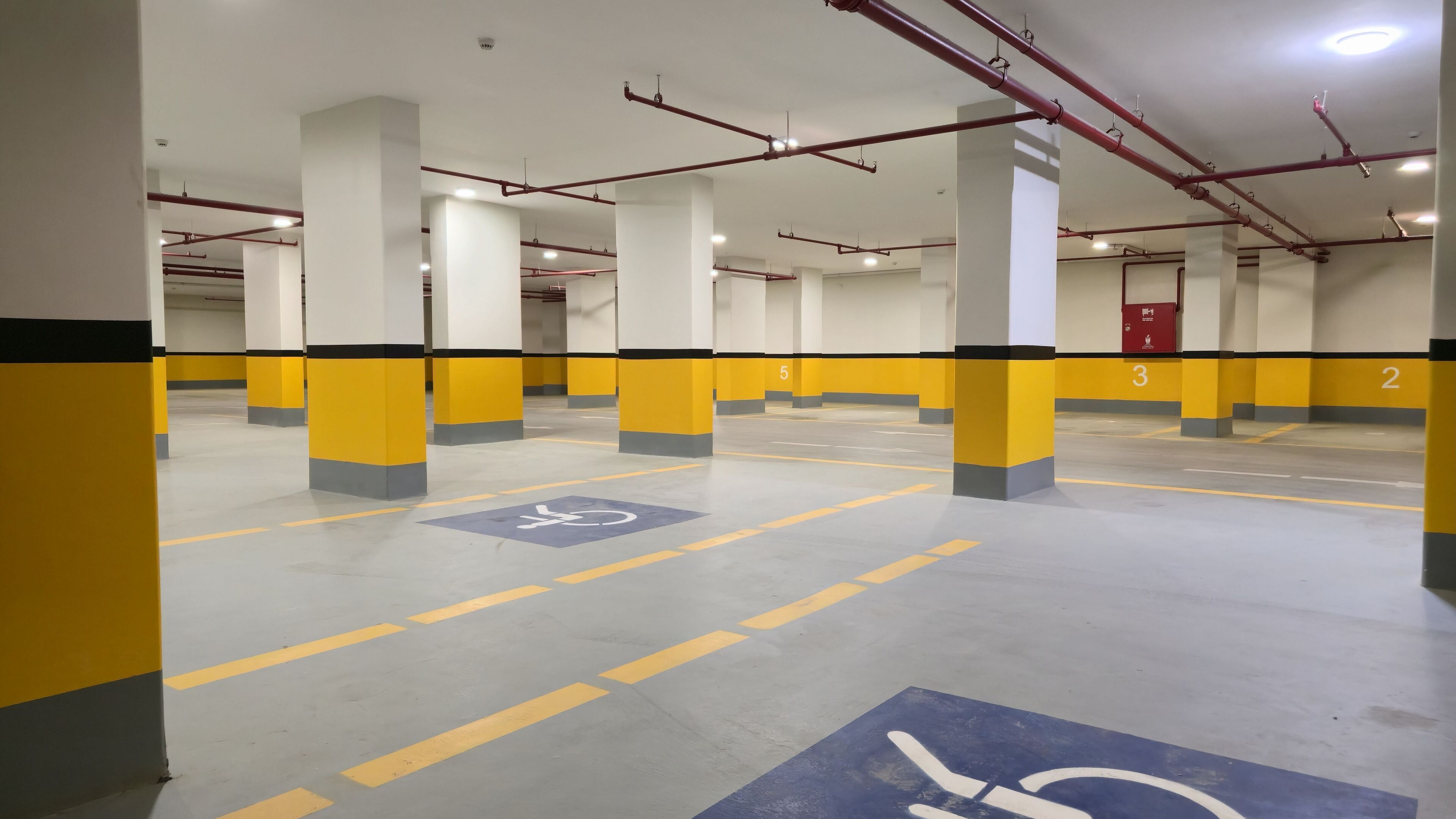 Un aparcamiento de varios niveles con pilares amarillo y gris, marcas de carril claras y una plaza de aparcamiento para discapacitados.