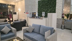 A modern lobby with grey sofas, a reception desk, and a green wall.