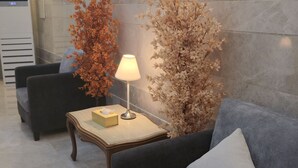 A modern lobby with a grey sofa, a small table with a lamp, and decorative plants.