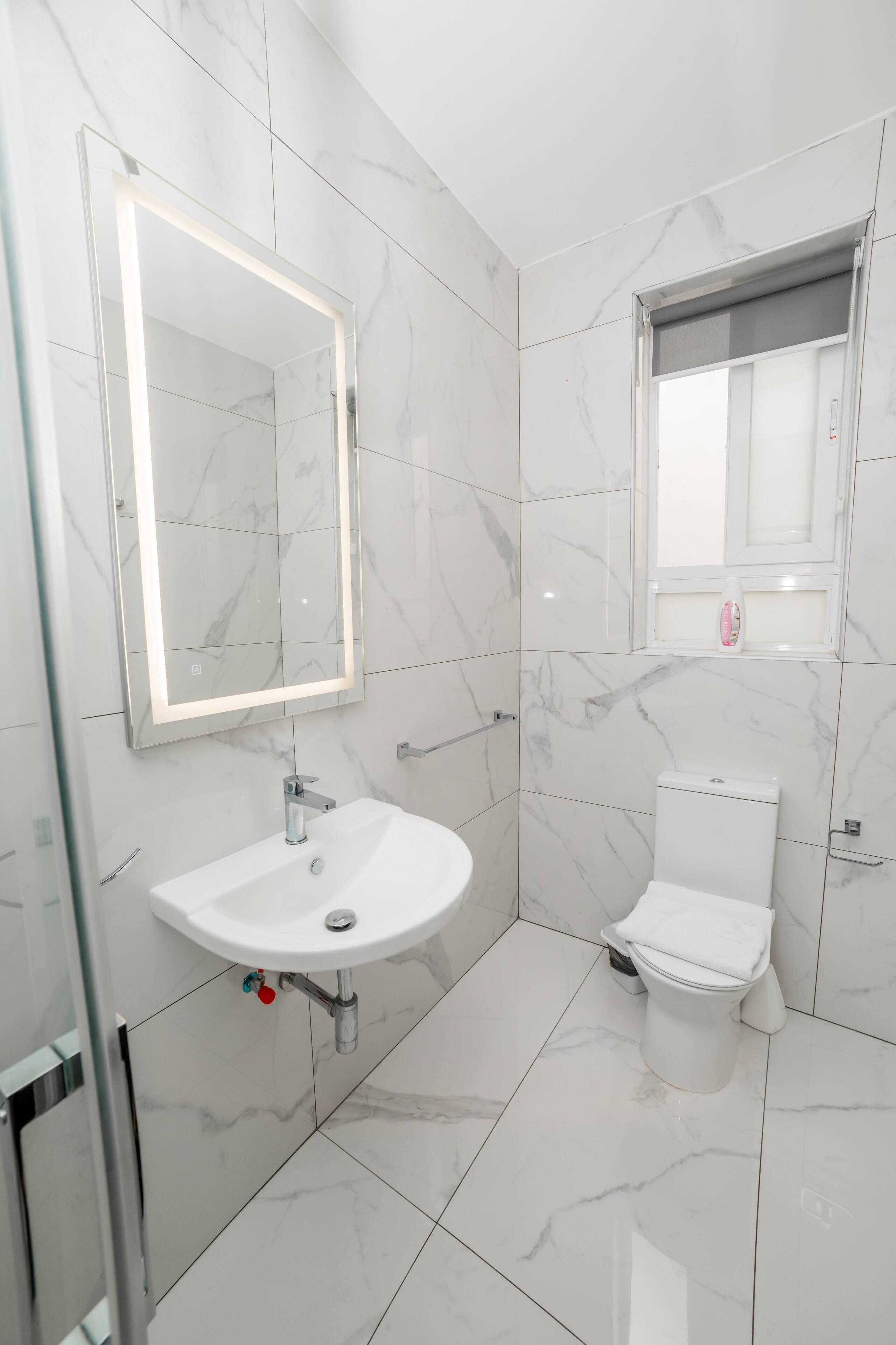 A modern bathroom with a white sink, a toilet, and a mirror with built-in lighting.