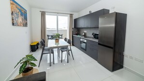 Een moderne keuken met een grote koelkast, donkere kasten en een eethoek met een tafel en stoelen.
