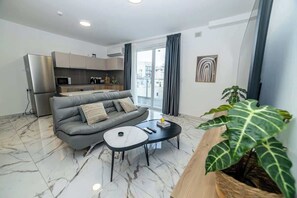 A modern living room with a grey sofa, a small coffee table, and a large plant. - Comfort Stay 1-Bedroom Apartment – by HostMT (San Pawl il-Baħar)