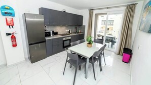 Una cocina moderna con armarios grises, un refrigerador de acero inoxidable y un comedor con una mesa blanca y sillas grises.