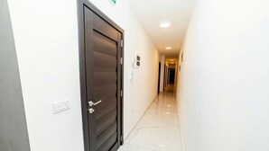 Un pasillo con una puerta de madera oscura, paredes blancas y un suelo de baldosas brillantes.