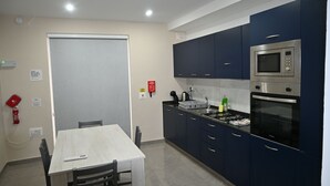 A kitchen with dark blue cabinets, a microwave, an oven, and a dining table with chairs. - Comfortable 3-Bedroom Seaside Stay (St. Paul's Bay)