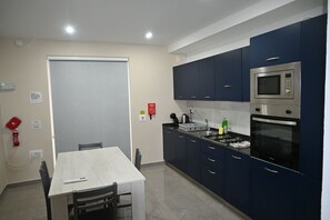 A kitchen with dark blue cabinets, a microwave, an oven, and a dining table with chairs. - Comfortable 3-Bedroom Seaside Stay (St. Paul's Bay)