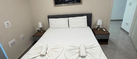 A hotel room with a large bed, two bedside tables with lamps, a painting on the wall, and a fire exit sign.
