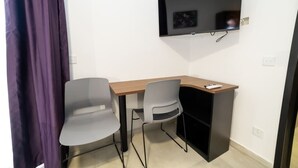 Une petite pièce avec un bureau, deux chaises, un téléviseur fixé au mur et un rideau violet.