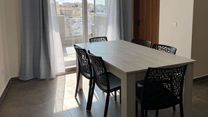 Ein Essbereich mit Tisch und Stühlen, eine Schiebeglasdoor und Blick auf Gebäude im Freien.