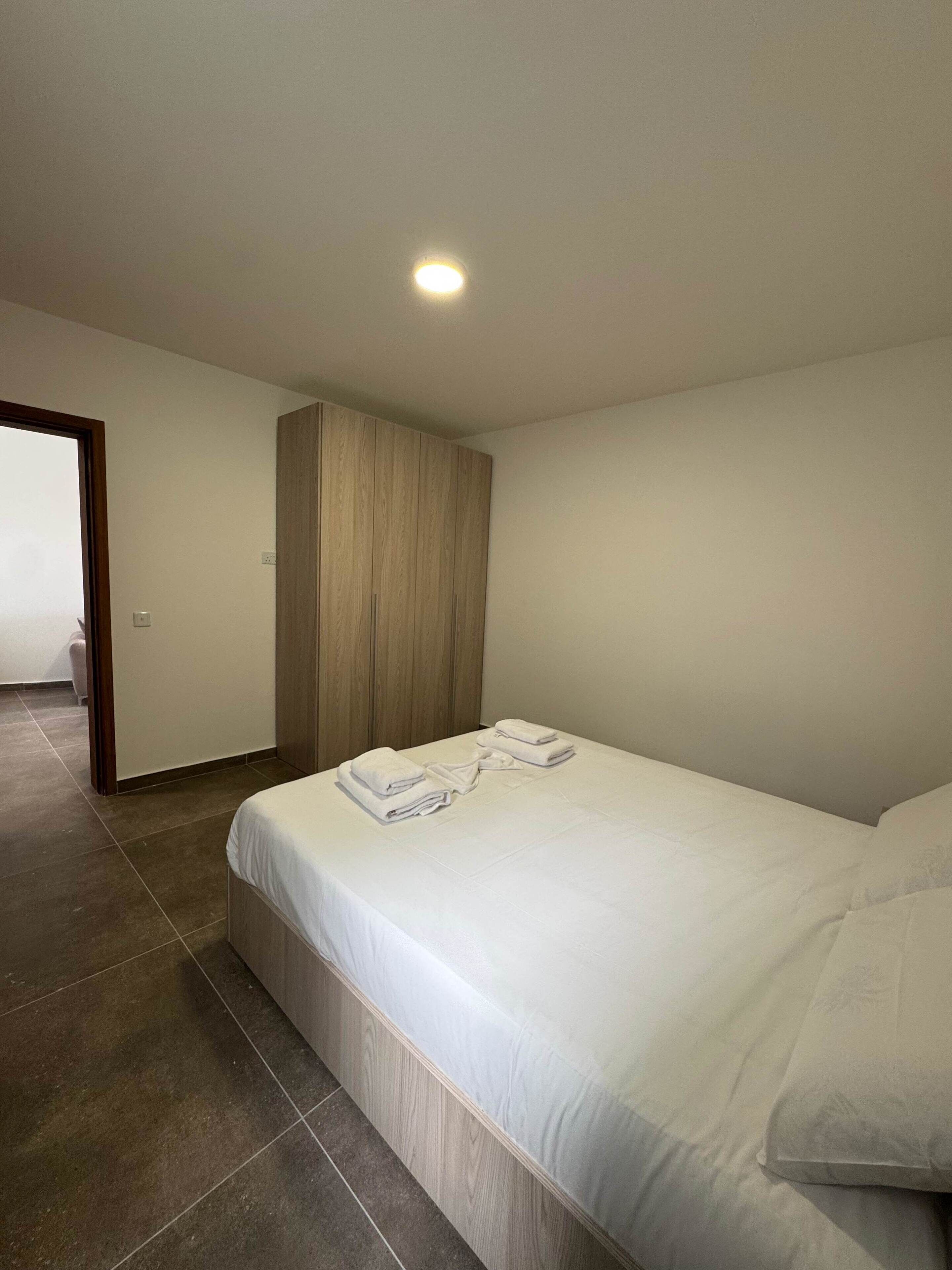 A hotel room with a bed, a wooden wardrobe, and a tiled floor.