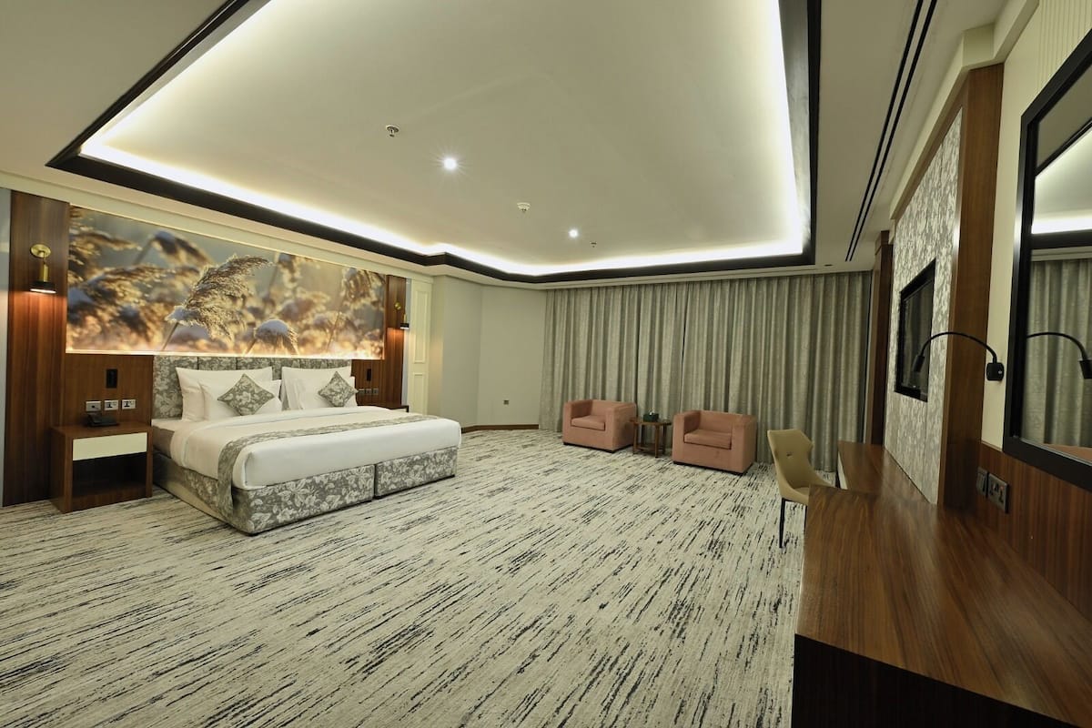 A modern hotel room with a large bed, two armchairs, a small table, and a large mirror.