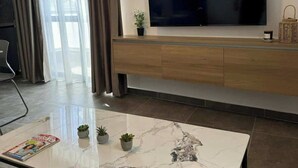 Un salon moderne avec un grand téléviseur à écran plat affichant le logo « NETFLIX », une console en bois, une table basse en marbre et une plante en pot.