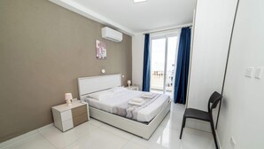 A modern bedroom with a bed, bedside tables, a chair, and a view of the outdoors. - Spacious 2BR Apartment with Terrace – by HostMT (San Pawl il-Baħar)
