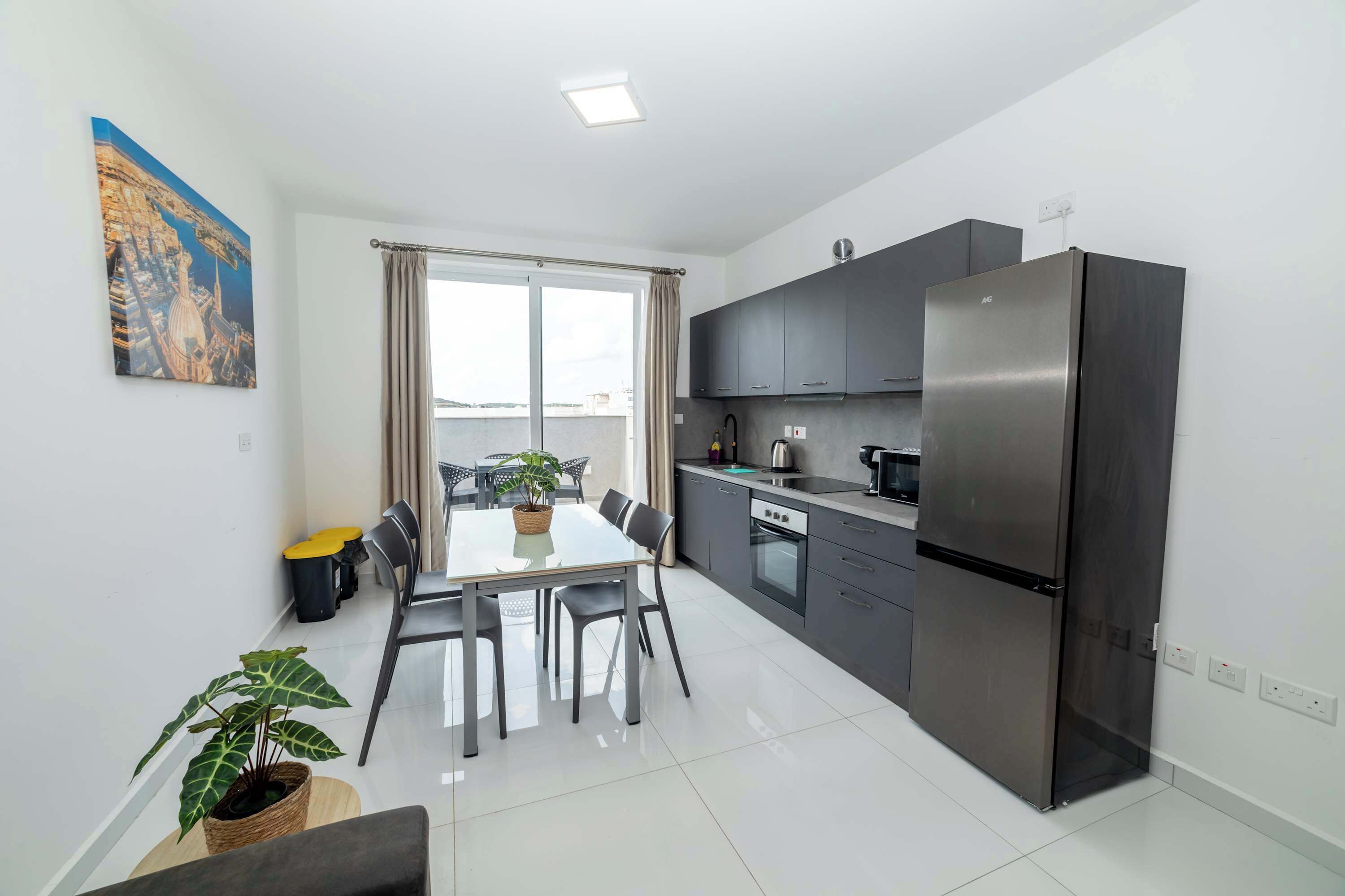 A modern kitchen with a stainless steel refrigerator, dark cabinets, and a dining area with a table and chairs.