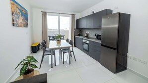 A modern kitchen with a stainless steel refrigerator, dark cabinets, and a dining area with a table and chairs. - Spacious 2BR Apartment with Terrace – by HostMT (San Pawl il-Baħar)