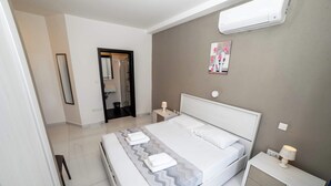 A modern hotel room with a large bed, a bedside table with a lamp, a wall-mounted air conditioner, and a bathroom visible through an open door. - Spacious 2BR Apartment with Terrace – by HostMT (San Pawl il-Baħar)