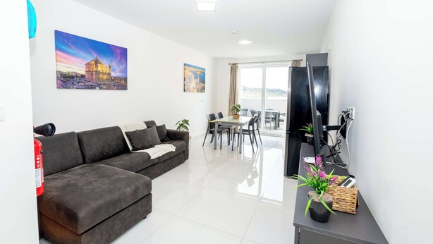 A modern living room with a sectional sofa, a dining area with a table and chairs, a flat-screen TV, and a balcony with a view. - Spacious 2BR Apartment with Terrace – by HostMT (San Pawl il-Baħar)