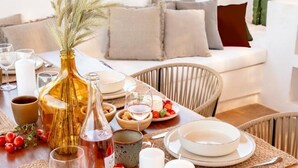 A dining table set with plates, glasses, and candles, surrounded by wicker chairs and a sofa.
