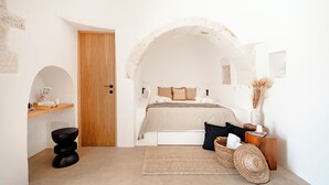 A bedroom with a wooden door, a bed with a beige blanket, a woven rug, and a basket.
