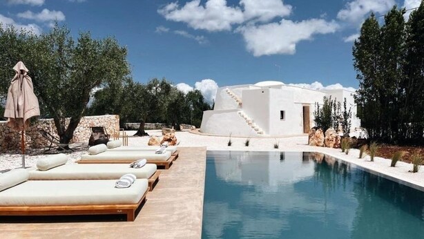 A poolside area with lounge chairs, a white building, and a clear sky.