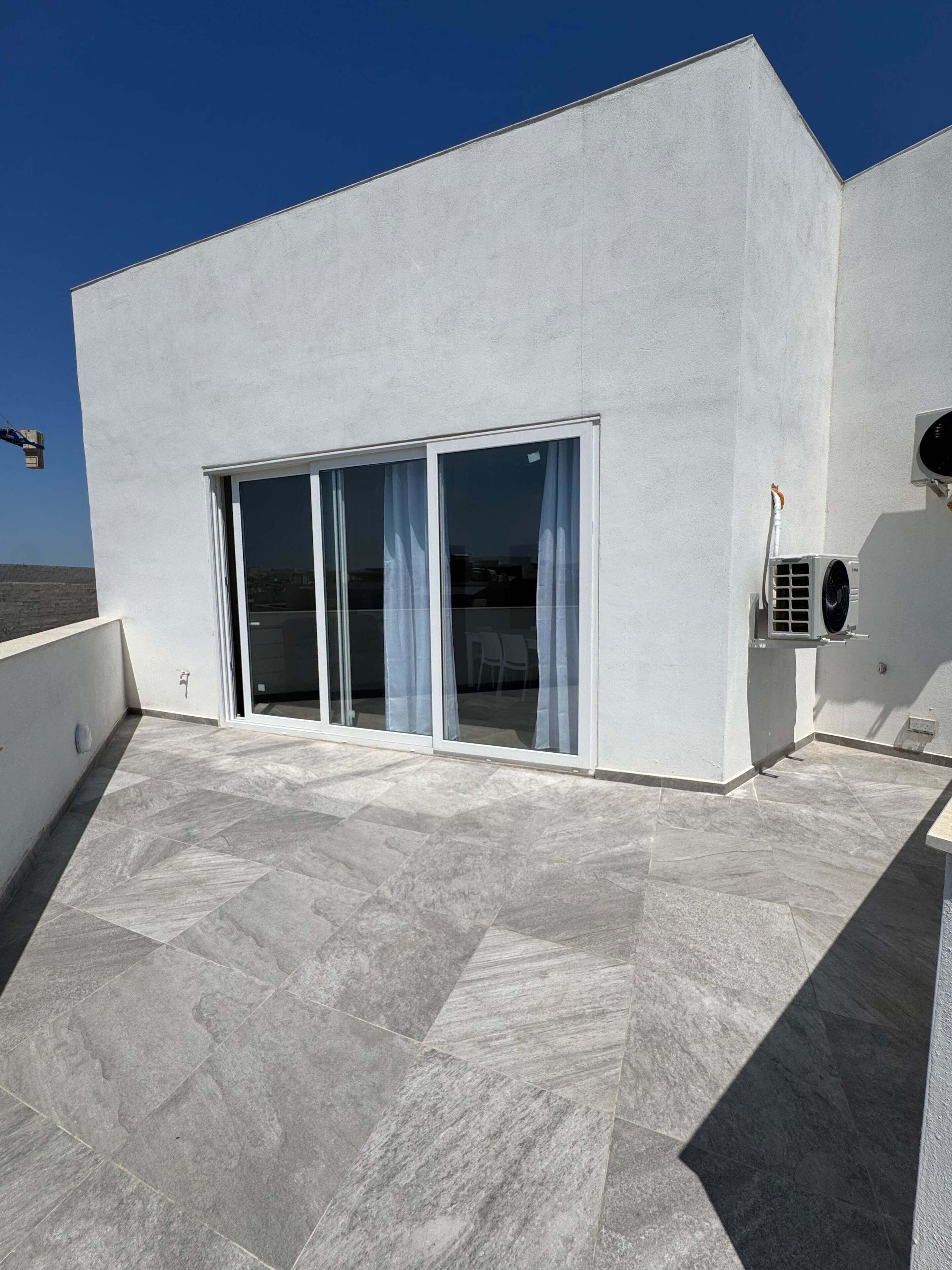 A modern building with a flat roof, large sliding glass doors, and an air conditioning unit.