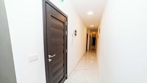 Um corredor com porta de madeira escura, parede branca e chão de mármore.