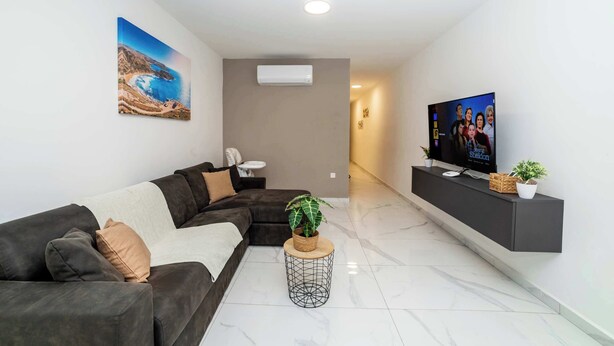 Uma sala de estar moderna com sofá seccional, TV de tela plana, planta em vaso e piso de mármore.