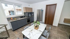 Une cuisine compacte avec un coin repas, un réfrigérateur et une fenêtre donnant sur un immeuble.