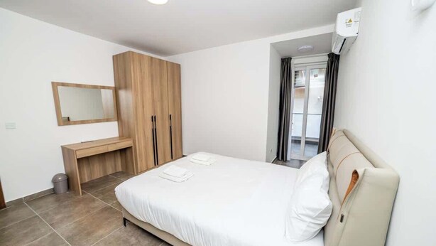Une chambre à coucher moderne avec un lit, une armoire en bois, un bureau et un miroir.