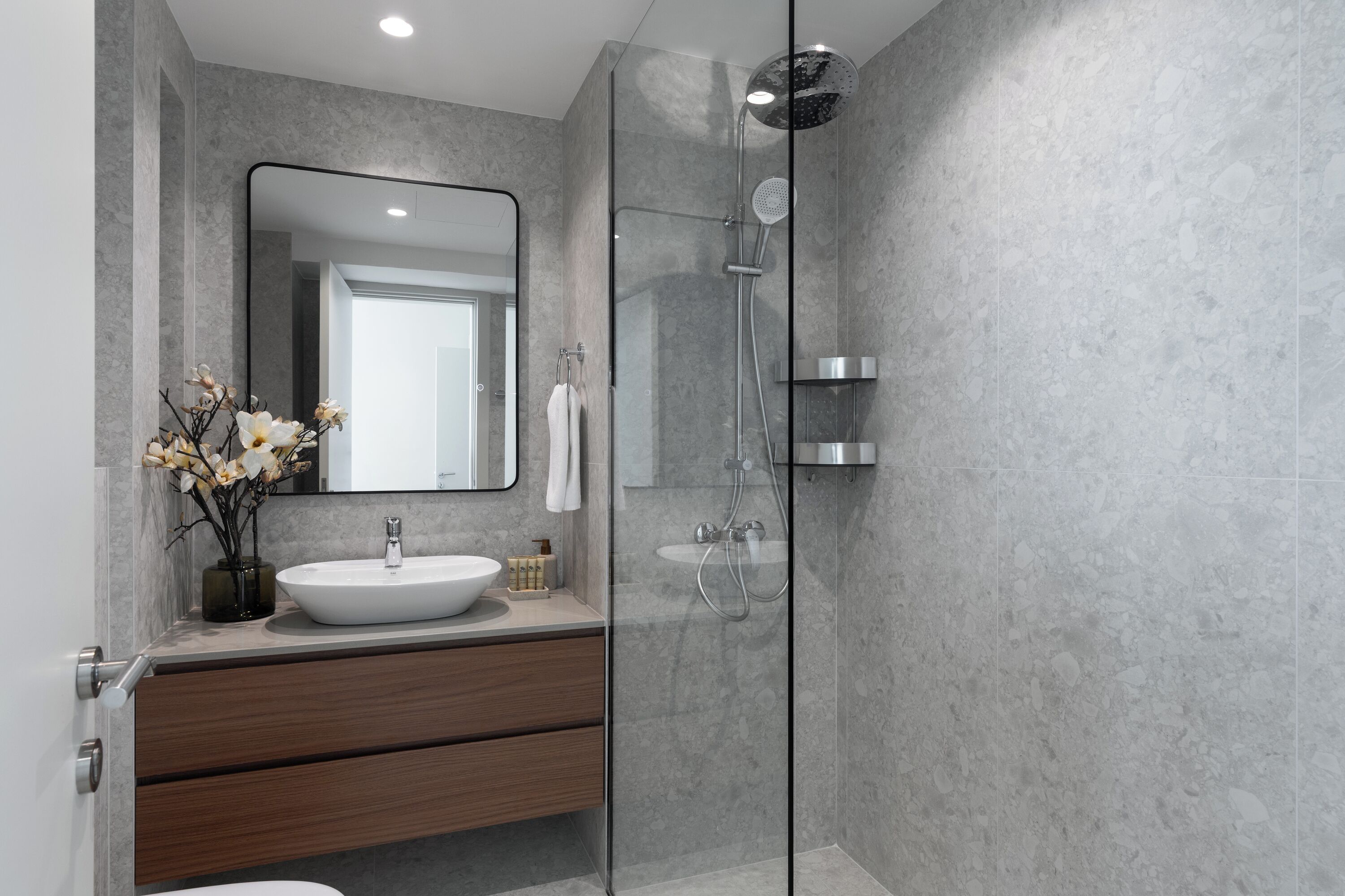 Un bany modern amb dutxa de vidre, un lavabo blanc i un mirall gran.