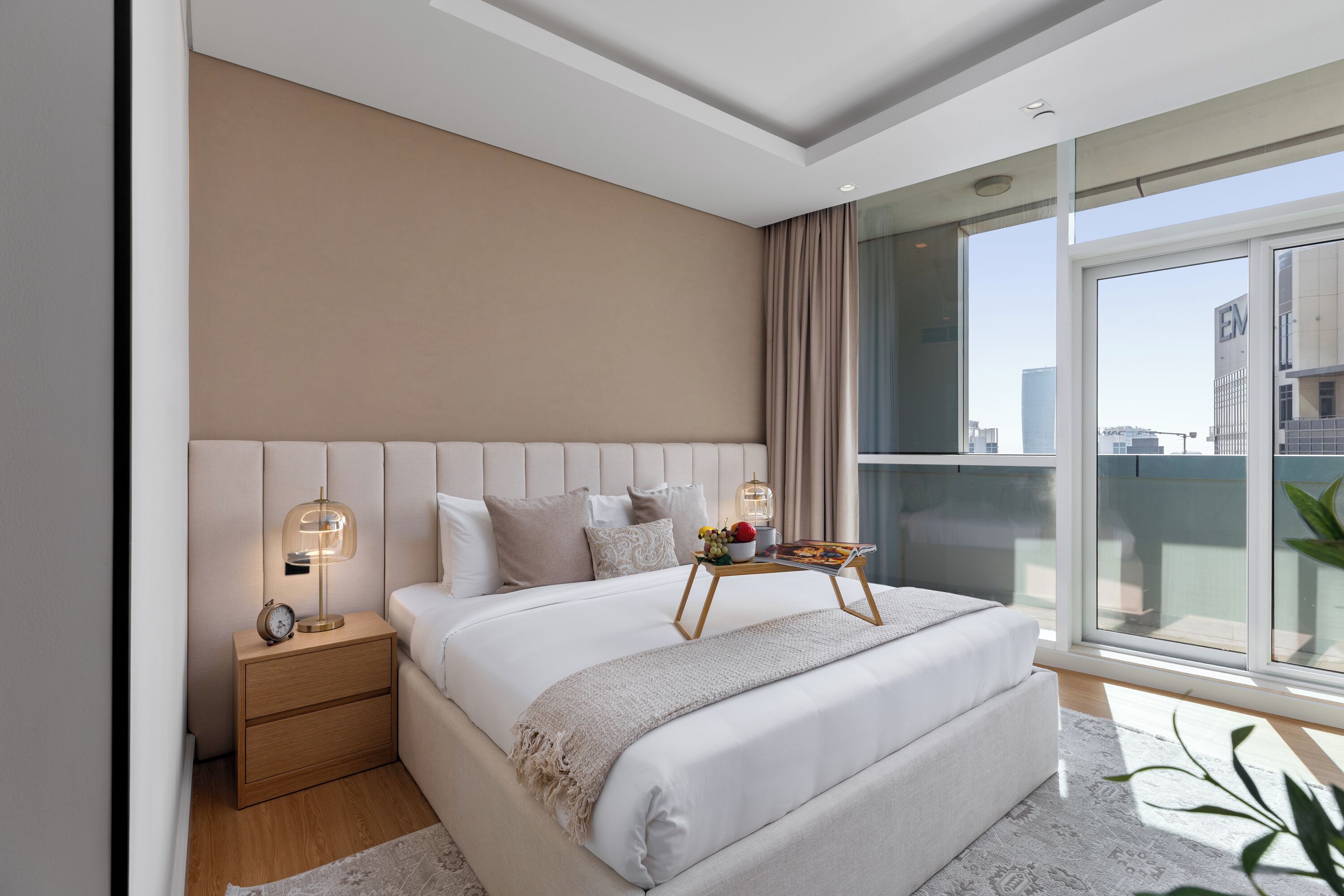 Een moderne slaapkamer met een groot bed, nachtkastjes, een bedlampje en uitzicht op de stad door grote ramen.