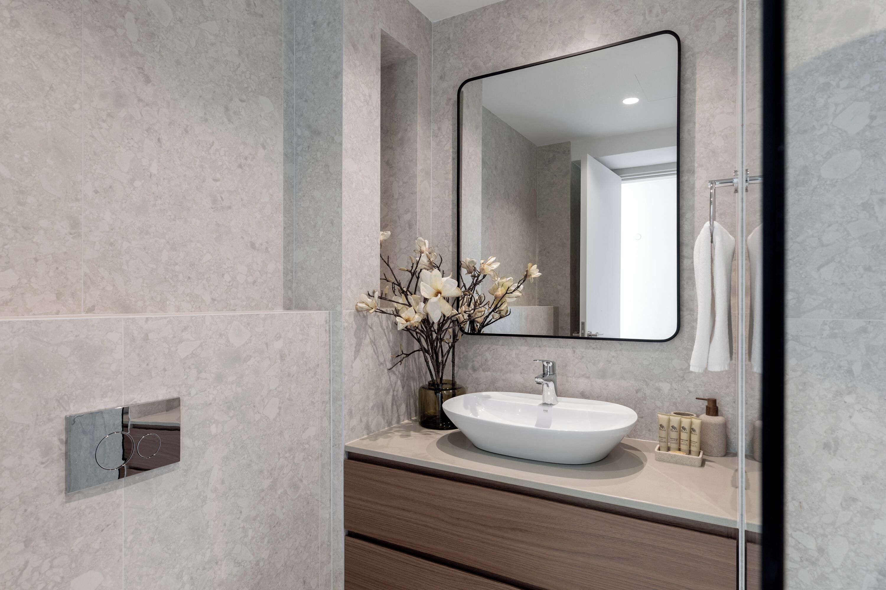 Une salle de bain moderne avec un grand miroir, un lavabo blanc et un vase rempli de fleurs.